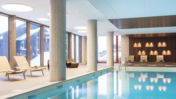 Un área de piscina interior moderna con sillones de descanso y vistas al exterior.
