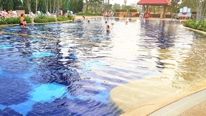 A large outdoor swimming pool with clear water, surrounded by lounge chairs and a covered seating area. - Studio Condo at Jomtien Beach (Pattaya)