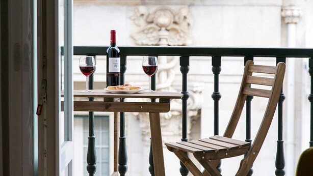 A balcony with a wooden table and chair, a bottle of red wine, and a glass of red wine. - JOIVY Sunny 1-bed flat w/terrace&sea view in Baixa,3mins to Arco da Rua Augusta (Lisboa)