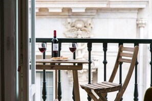 Ein Balkon mit Holztisch und Stuhl, einer Flasche Rotwein und einem Weinglas.