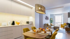 A modern kitchen with a dining area, featuring a wooden table with yellow chairs, a hanging light fixture, and a view of a balcony. - JOIVY Sunny 1-bed flat w/terrace&sea view in Baixa,3mins to Arco da Rua Augusta (Lisboa)