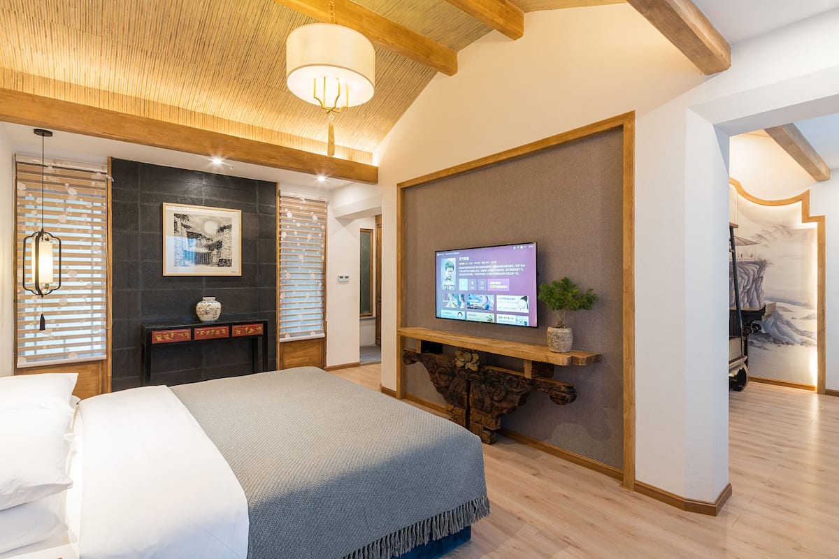 Une chambre d’hôtel moderne avec un grand lit, un téléviseur fixé sur une console en bois et une cheminée.