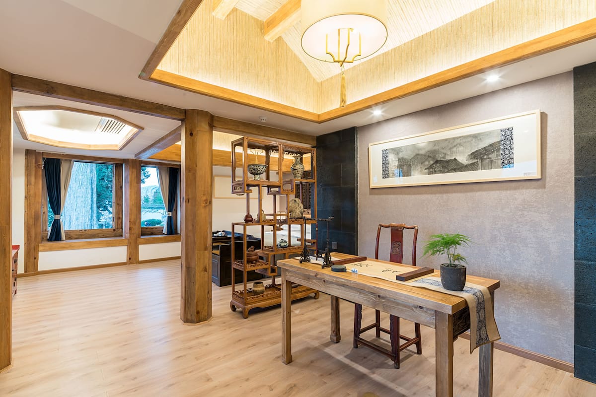 Une pièce spacieuse avec des poutres en bois, une grande table et une étagère de style asiatique traditionnel où sont exposées des poteries.