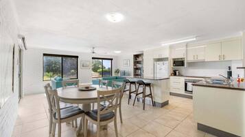 A modern kitchen with white cabinets, a dining area with a round table and chairs, and a view of greenery outside.