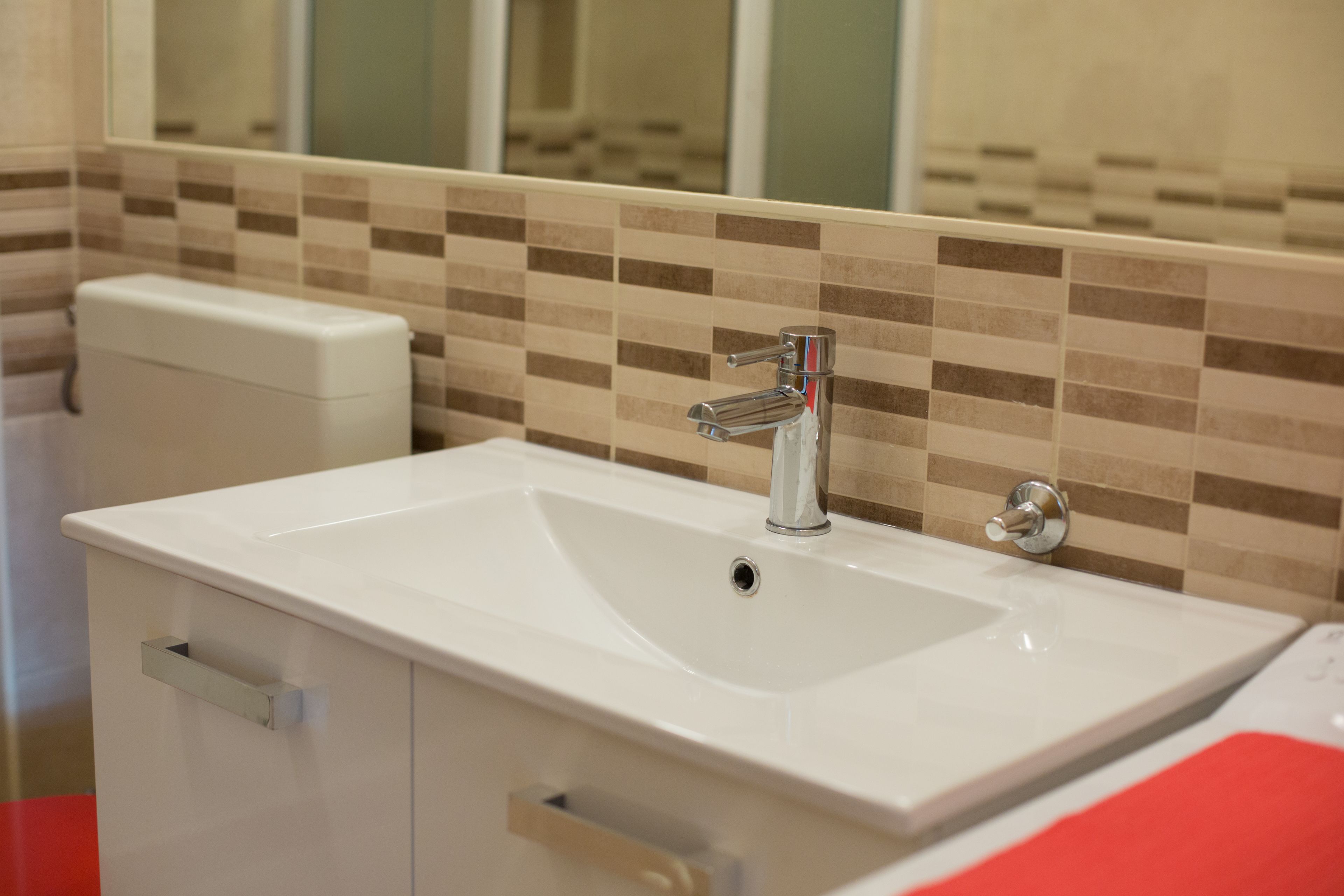 Un baño con lavamanos blanco, grifo cromado y un rebozo de azulejos.