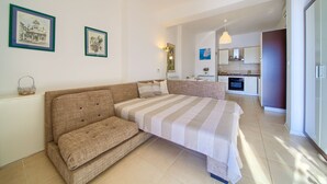 A modern bedroom with a large bed, a sofa, and a kitchenette in the background. - Apartments Six (Kraljevica)
