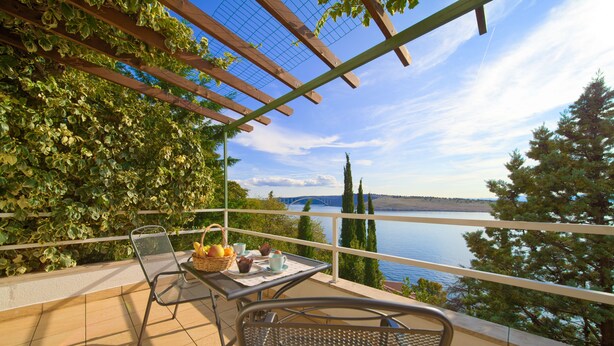 A balcony with a table set for breakfast, overlooking a body of water and a distant bridge. - Apartments Six (Kraljevica)