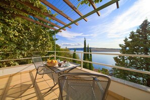 A balcony with a table set for breakfast, overlooking a body of water and a distant bridge. - Apartments Six (Kraljevica)