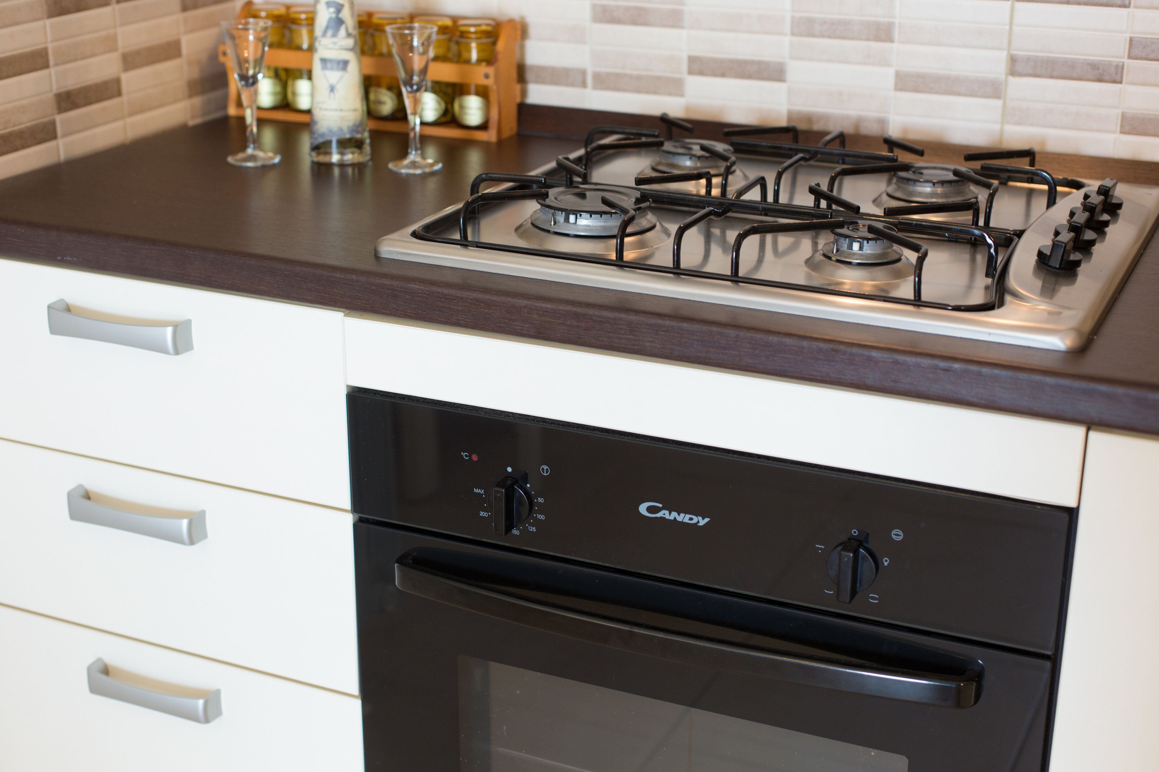 A kitchen with a gas stove, oven, and a wine rack with glasses.