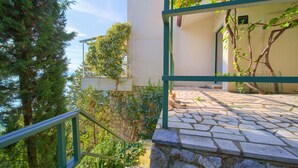 A stone staircase leading to a balcony with a green railing, surrounded by greenery and a clear sky. - Apartments Six (Kraljevica)