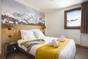 A hotel room with a bed, a nightstand, a window with curtains, and a mountain landscape mural on the wall.