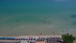 A beach with clear turquoise water, people swimming and sunbathing, and rows of umbrellas and beach chairs along the shore. - Porto Thassos (Thasos)