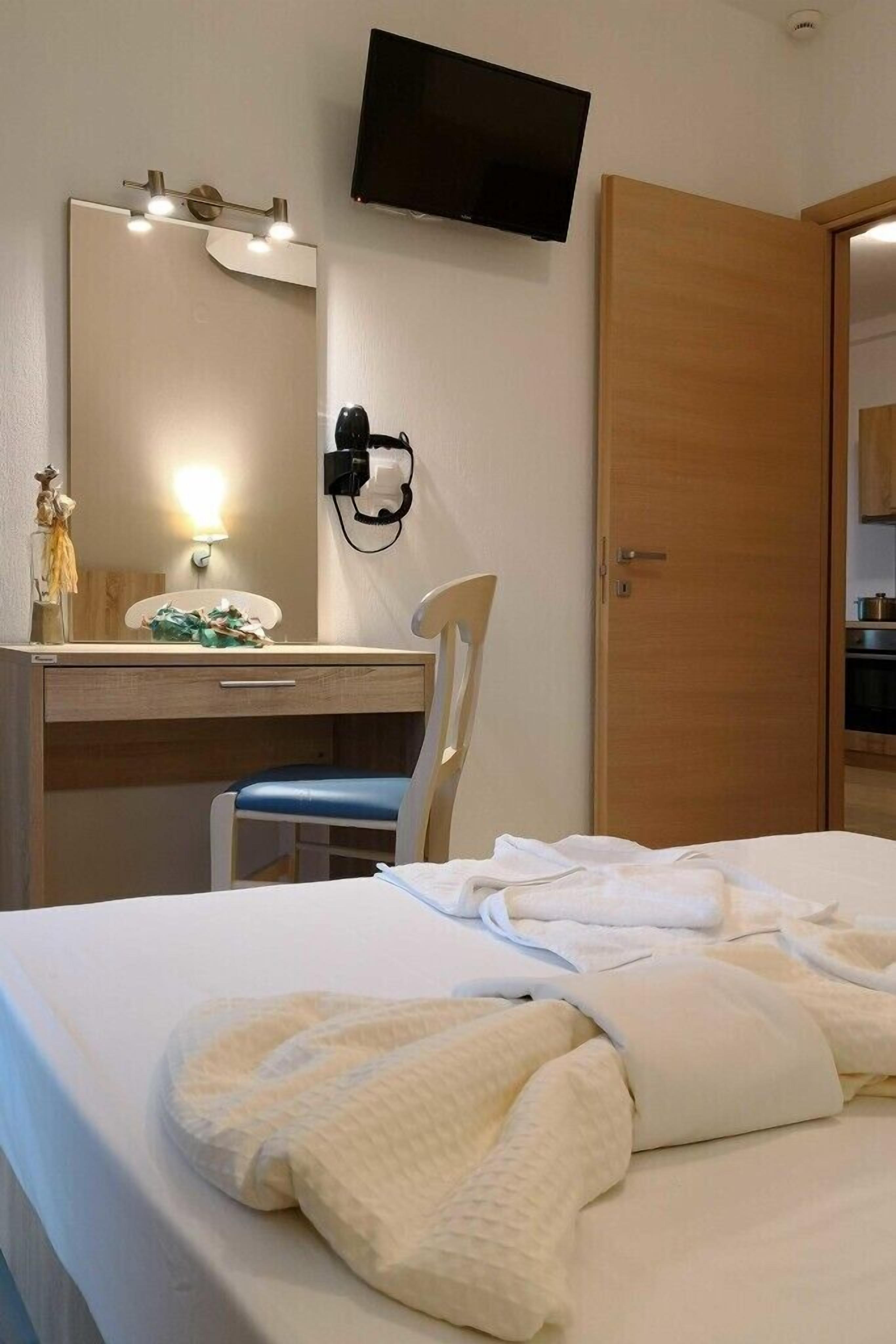 A hotel room with a bed, a desk with a chair, a television mounted on the wall, and a wooden door.