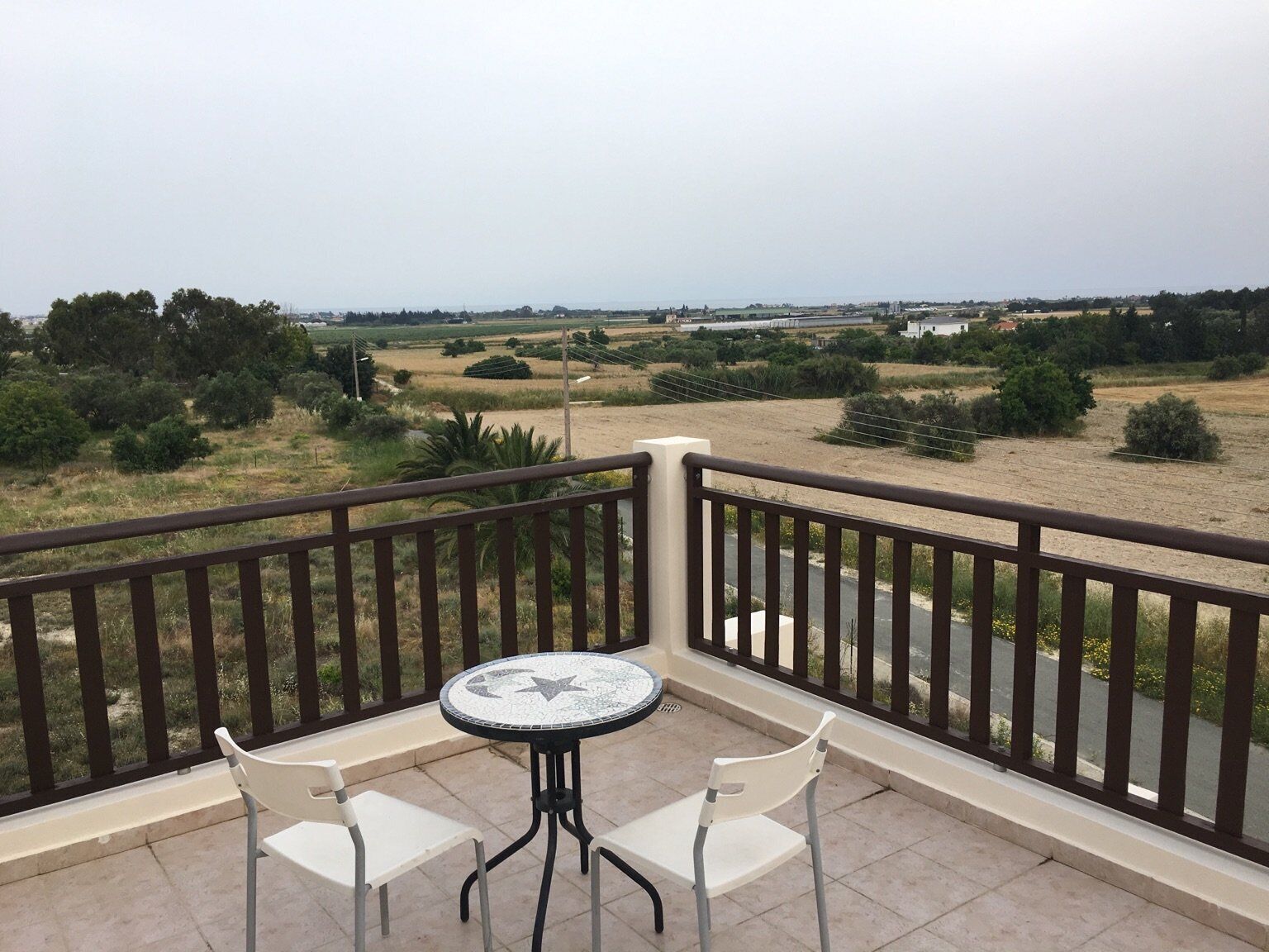 A balcony with a tiled floor, two white chairs, and a round table with a mosaic top.