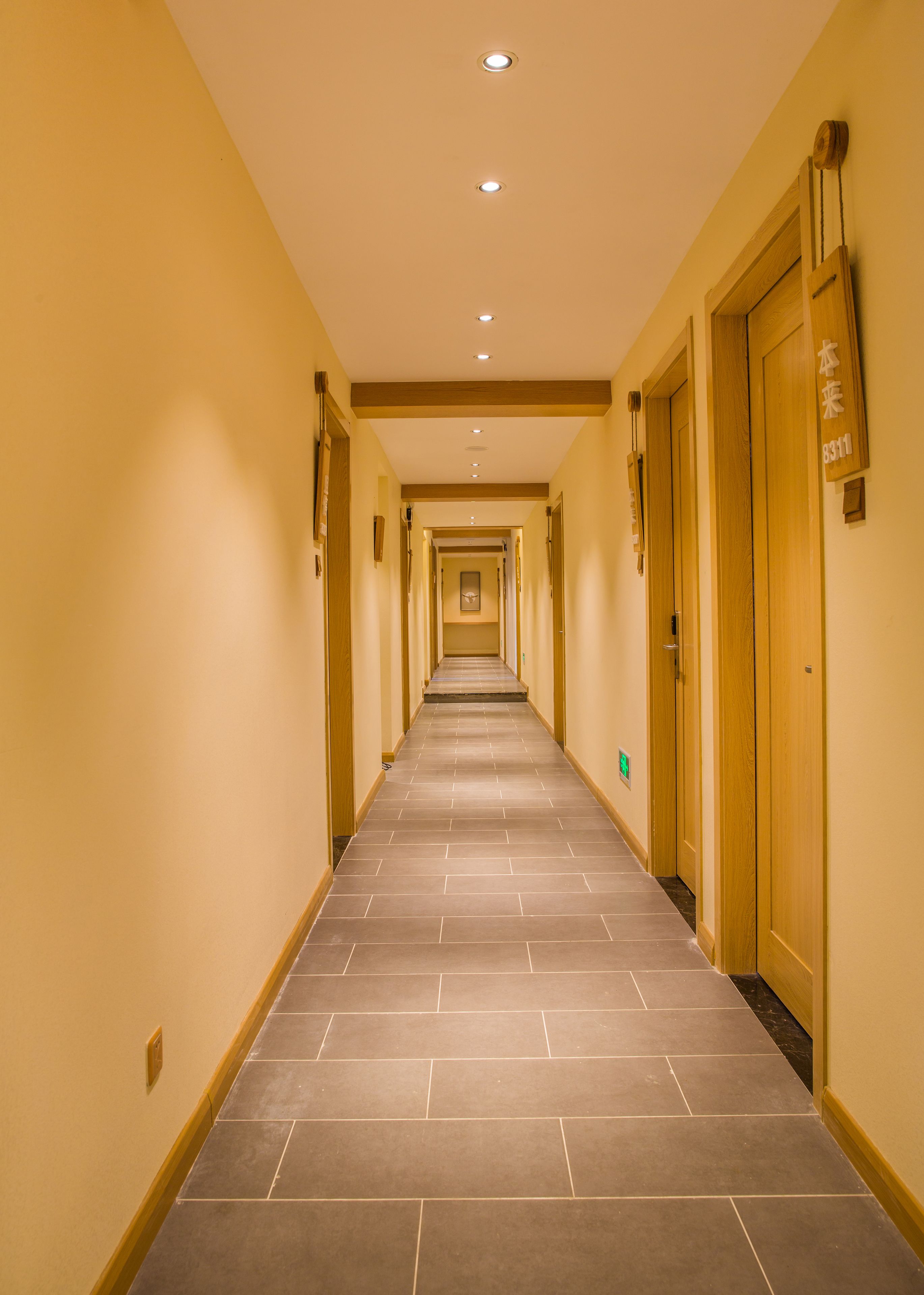 Un couloir d’hôtel avec un sol carrelé, des portes en bois et un éclairage encastré.