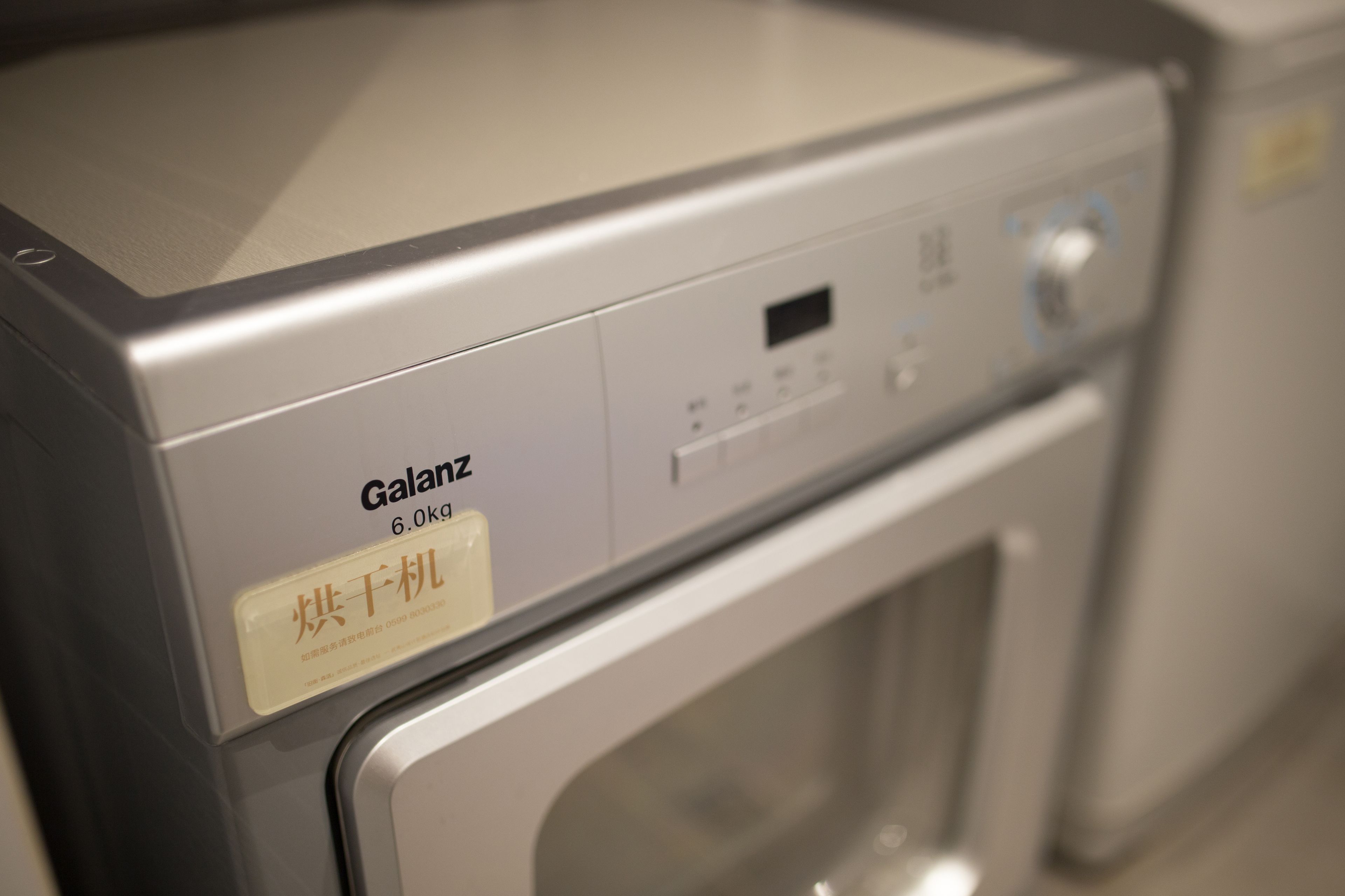 Een voorweergave van een Galanz wasdroger van 6,0 kg met een bedieningspaneel en een etiket in een vreemde taal.