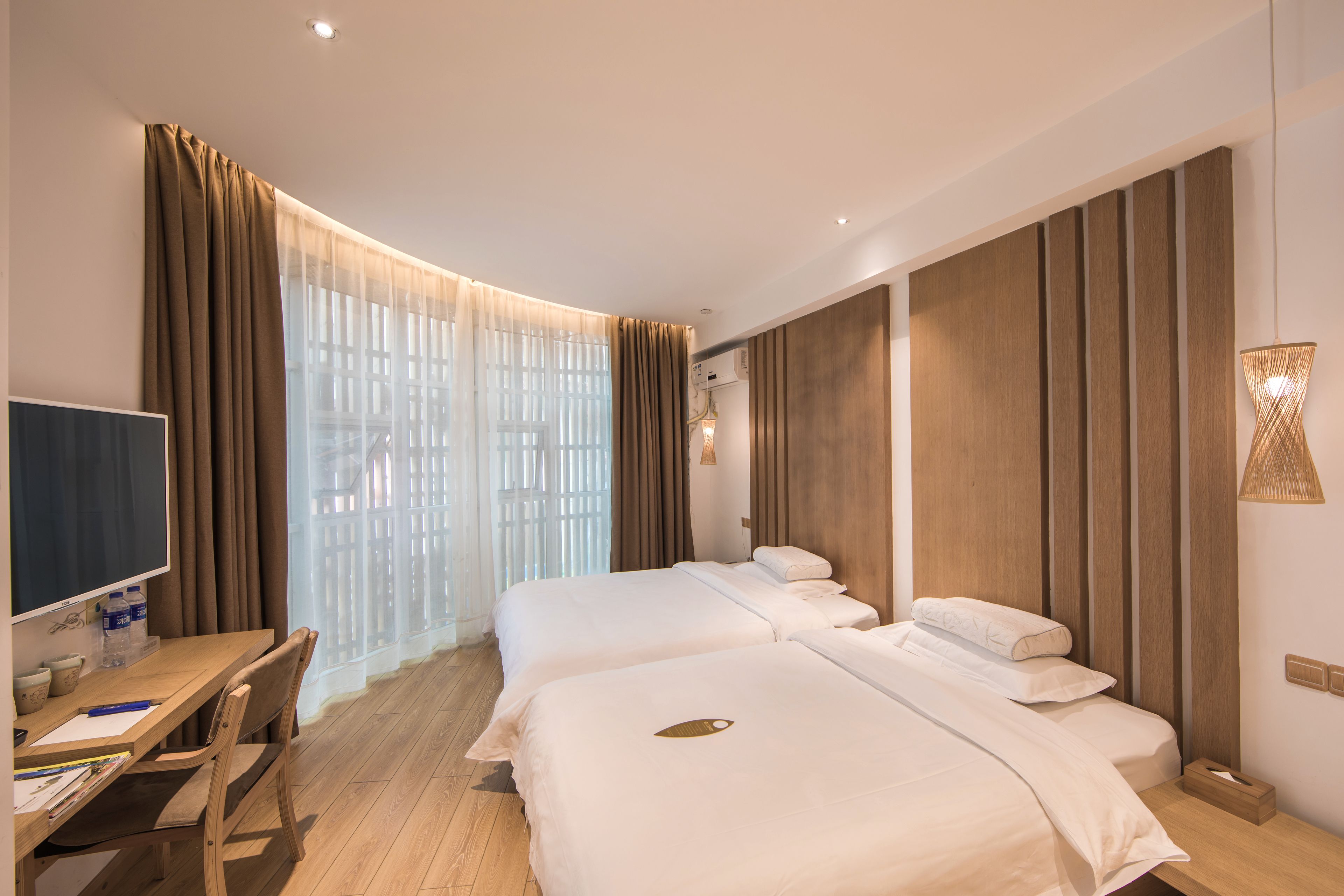 A hotel room with two beds, a desk, a chair, a TV, and a window with curtains.
