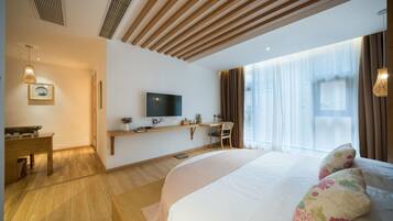 Habitación de hotel moderna con una cama grande, un escritorio, un televisor y una ventana con cortinas.