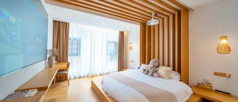 Una habitación de hotel moderna con una cama grande, listones de madera en el techo, un escritorio con computadora y un ventanal con cortinas.