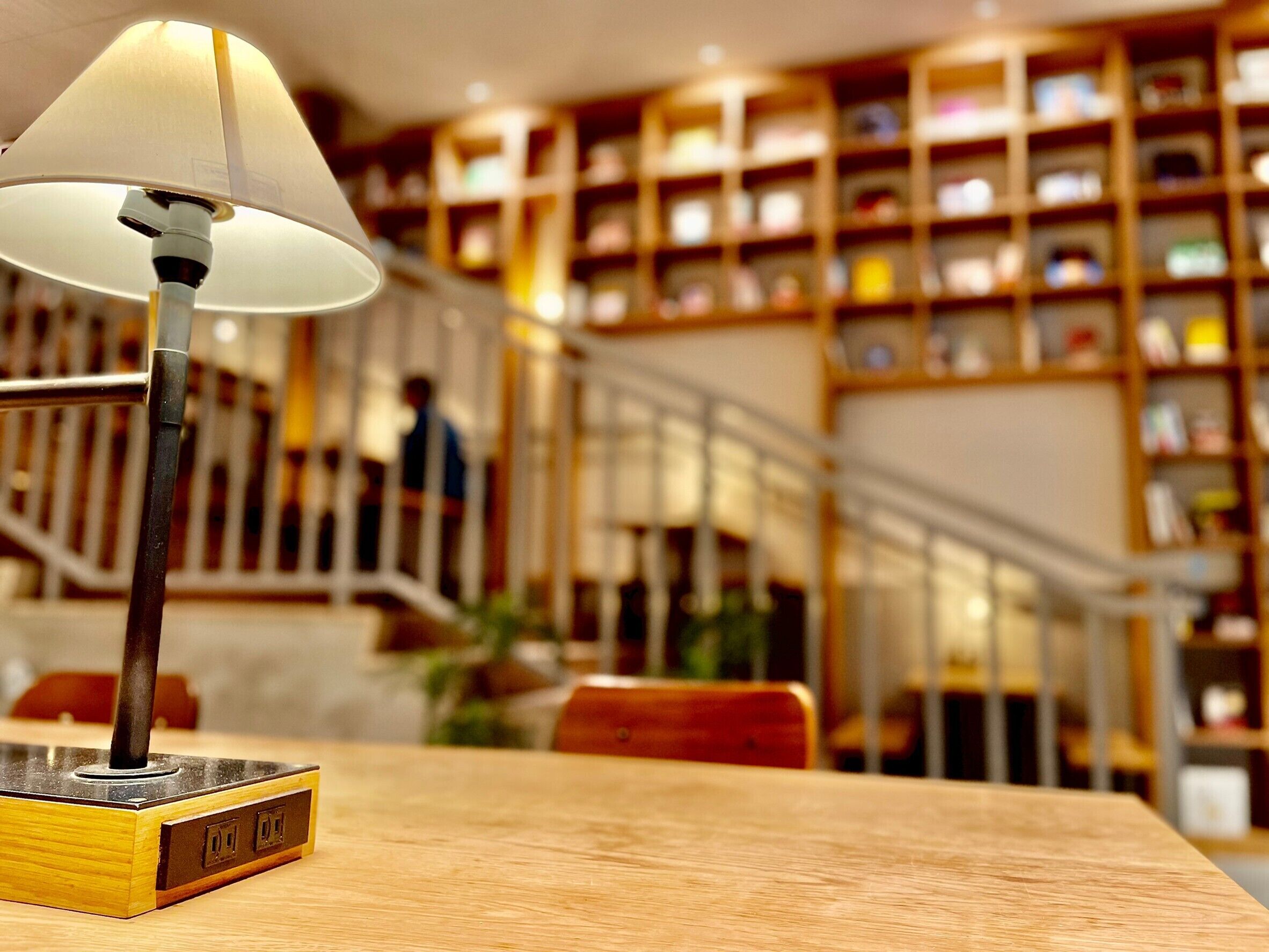 A lamp on a wooden table with a bookshelf in the background.