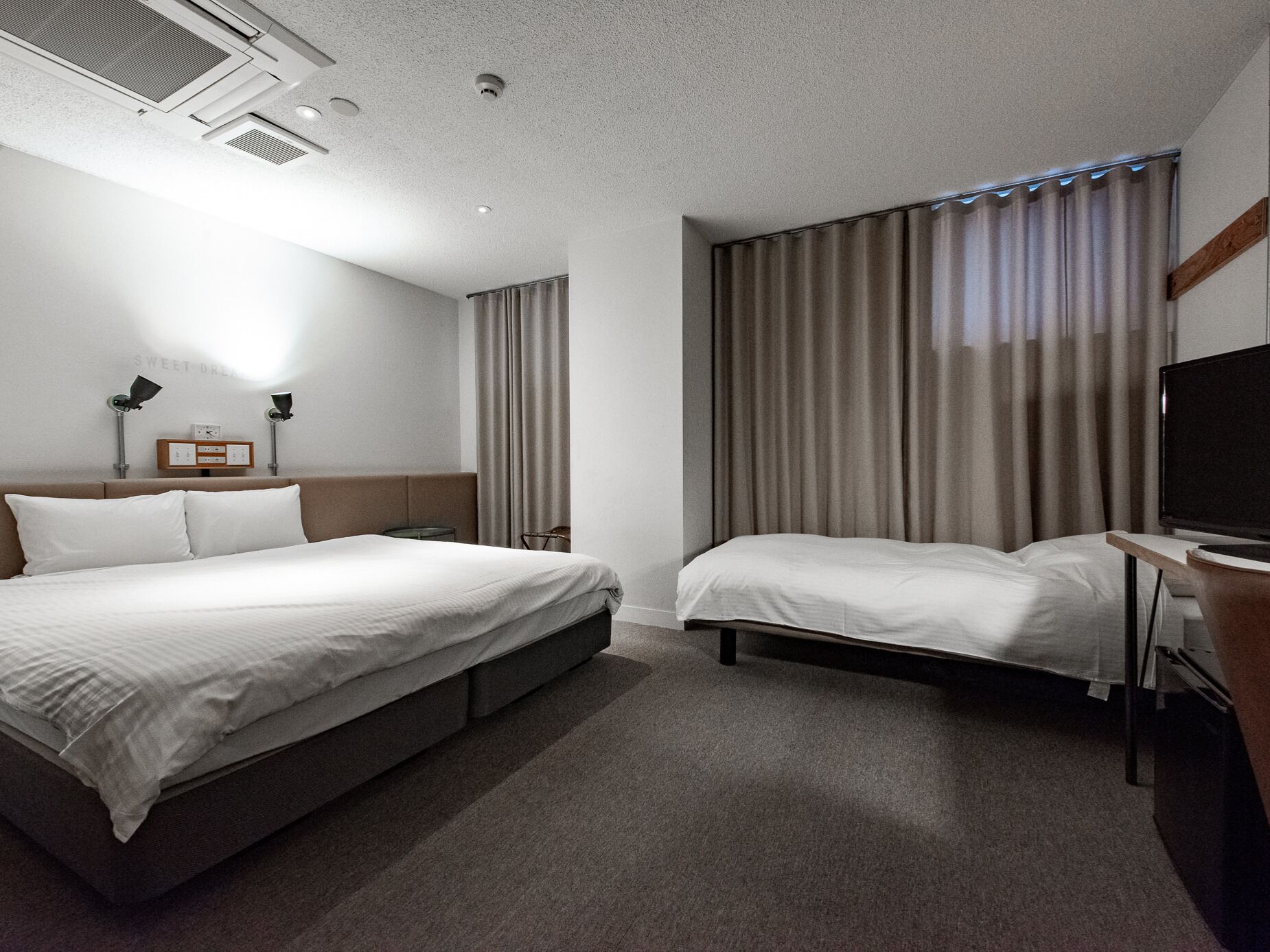 A hotel room with two beds, a flat-screen TV, and a desk.