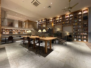 A spacious library with a central wooden table and chairs, surrounded by bookshelves filled with books. - Hotel Relief Kokura Annex (Kitakyushu)