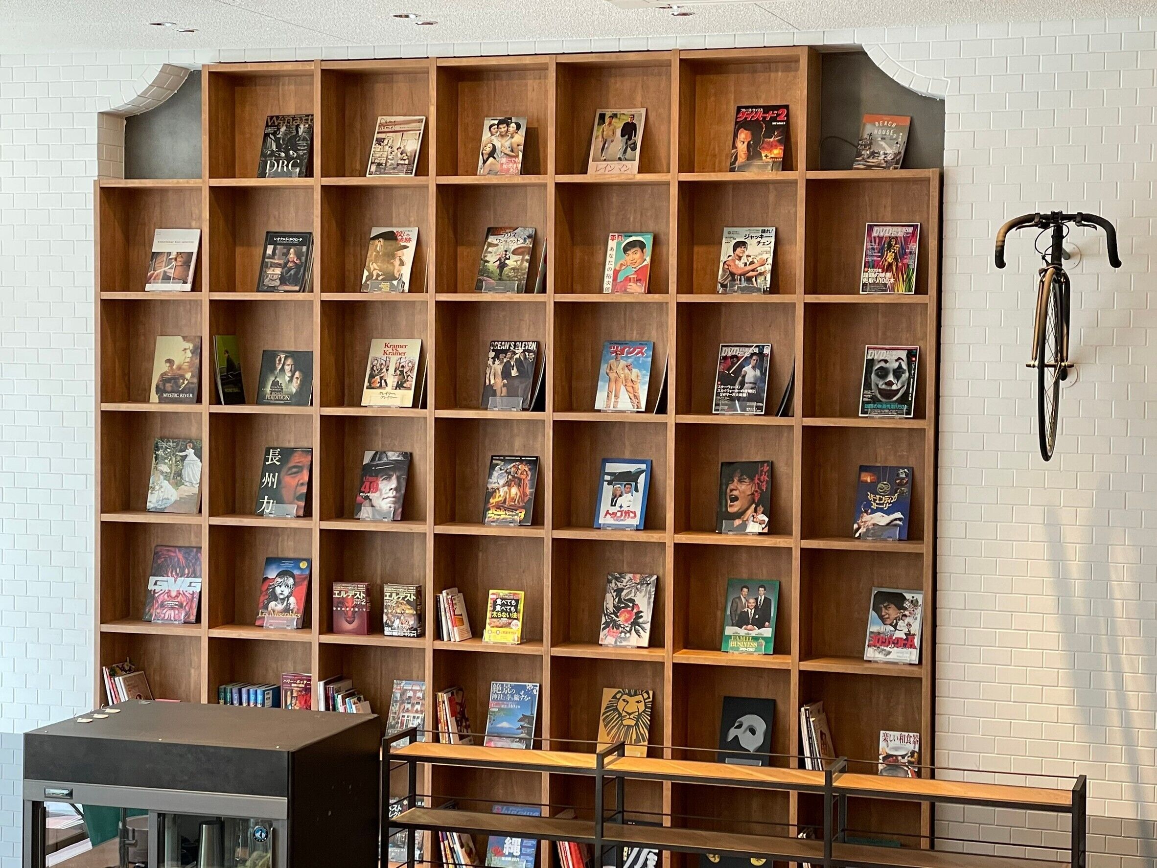 A bookshelf filled with various books and magazines, a bicycle hanging on the wall, and a small table in the foreground.
