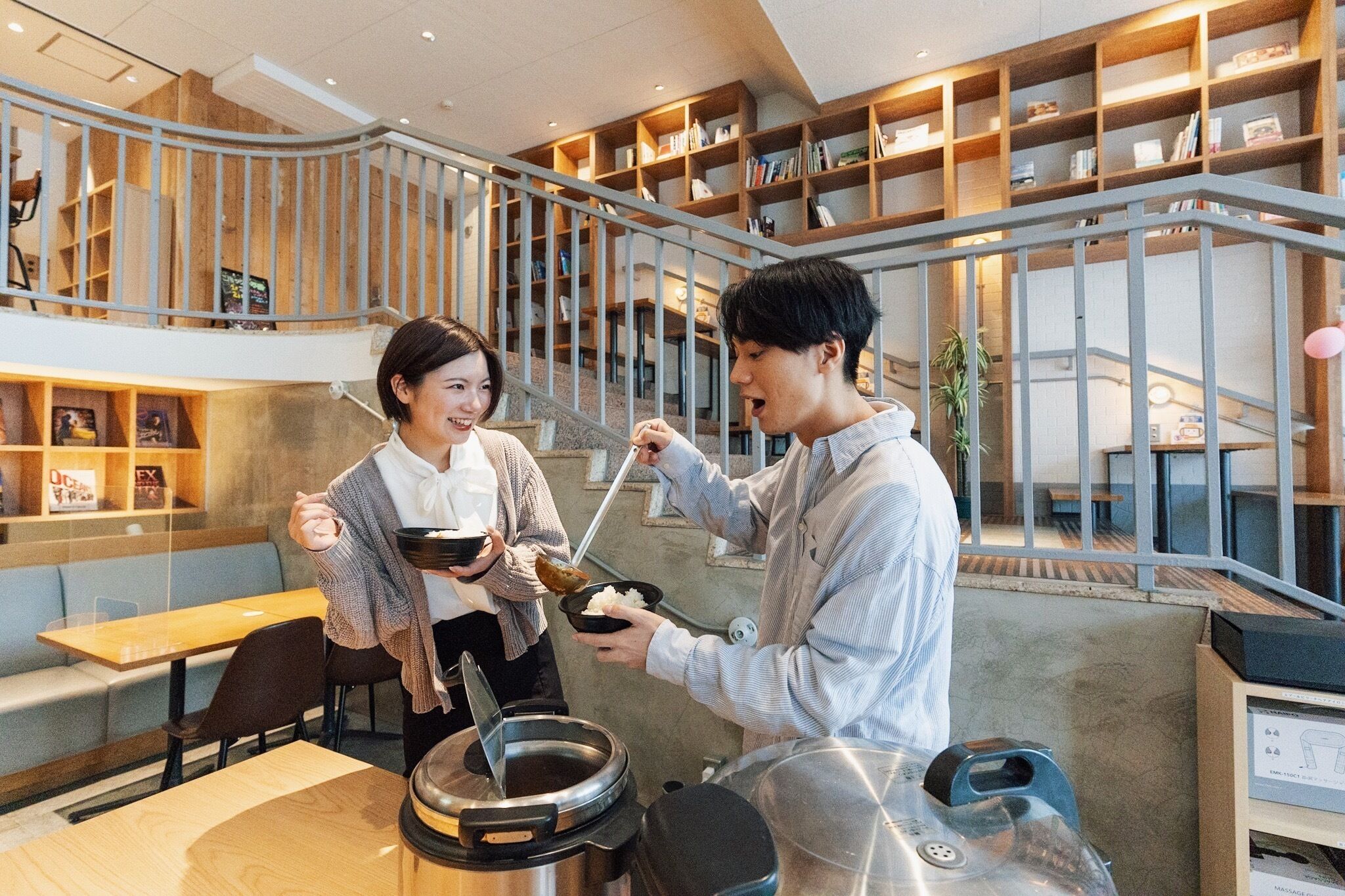 A restaurant with a modern interior, including a staircase, bookshelves, and a dining area with tables and chairs.