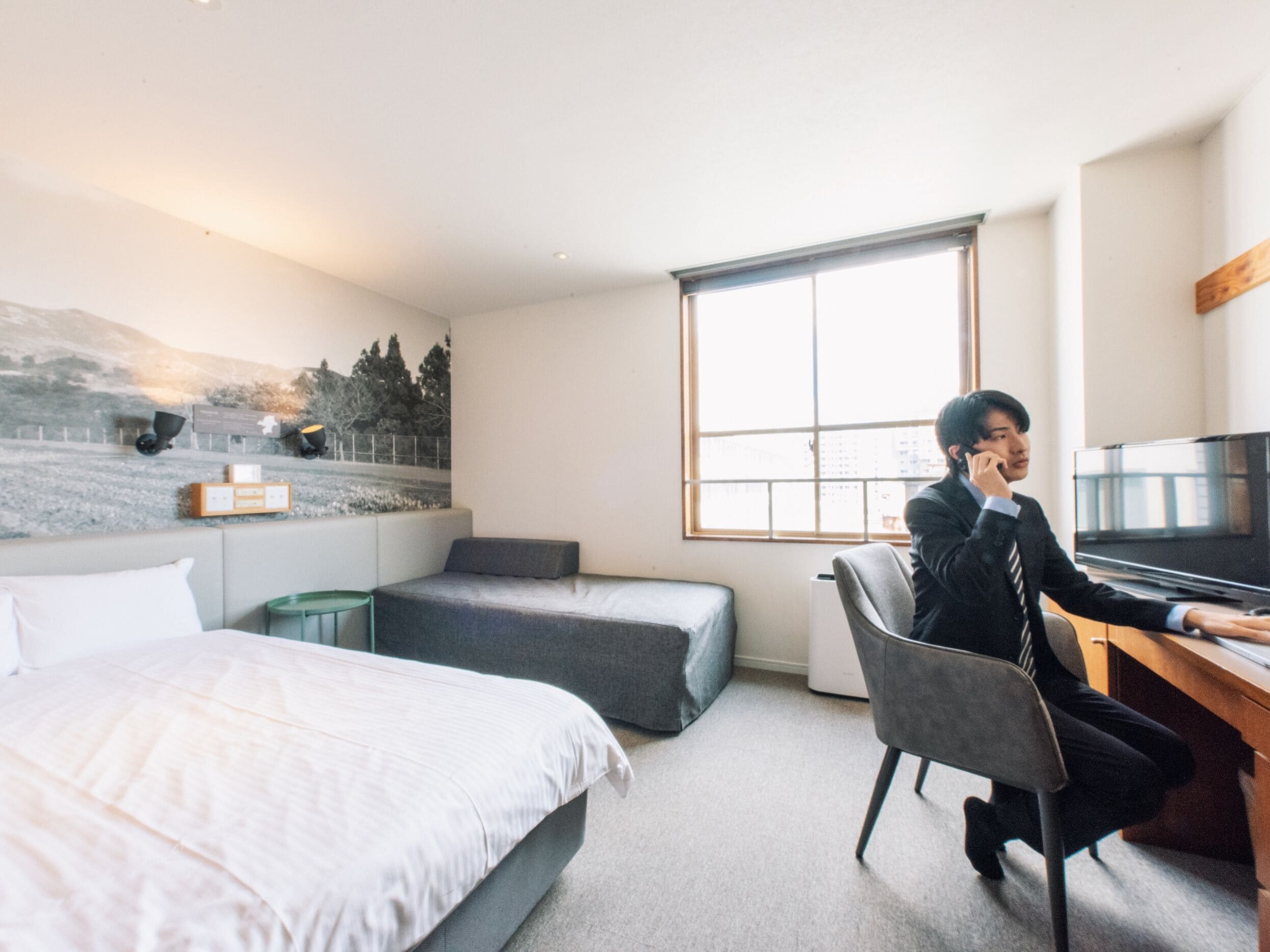 A hotel room with a bed, a desk, a chair, a television, and a window with a city view.