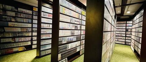 Una biblioteca con estanterías dispuestas en filas, un suelo cubierto de alfombra verde y elementos estructurales de madera.
