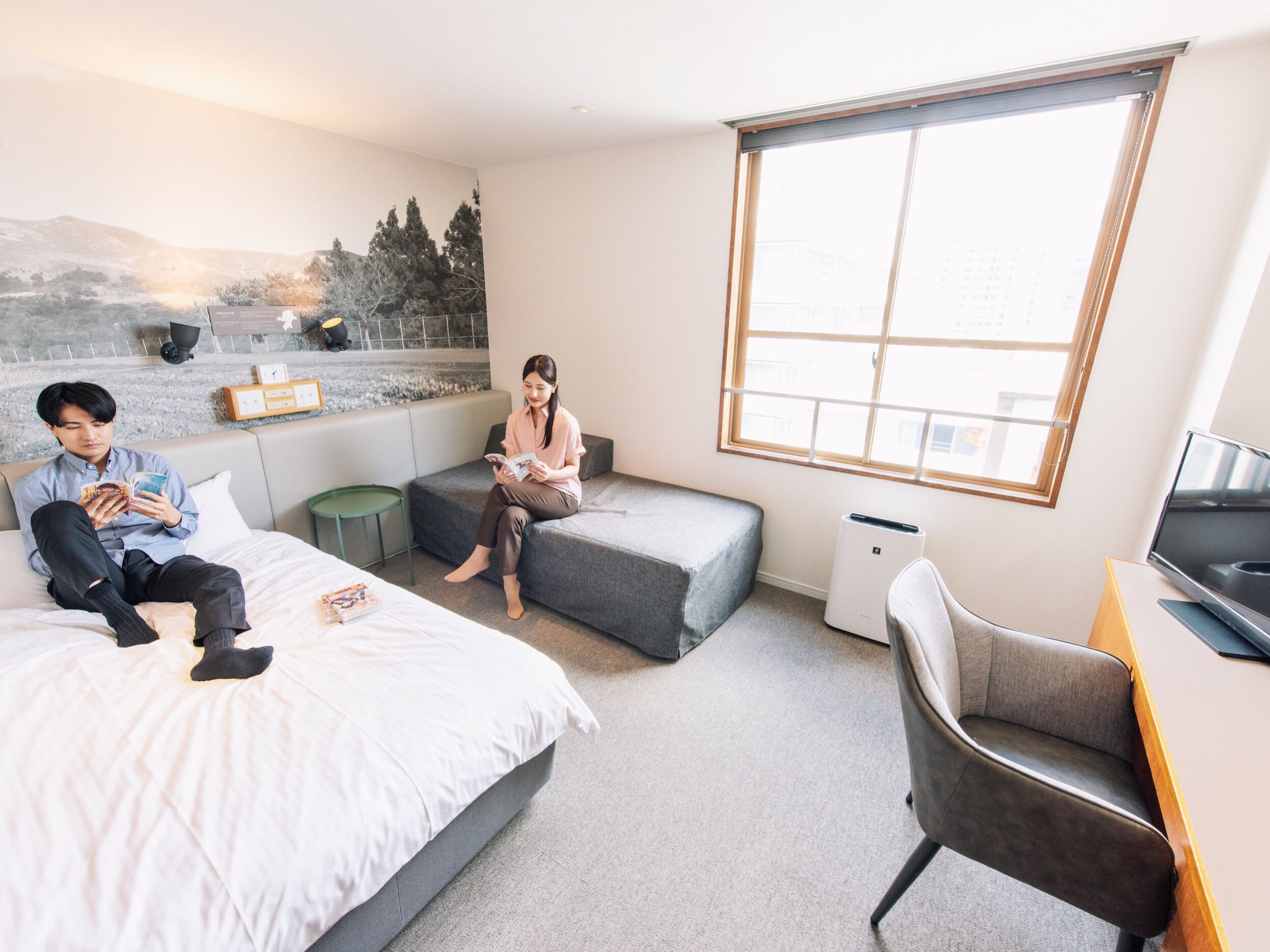 A modern hotel room with a large window, a bed, a sofa, a desk, and a chair.