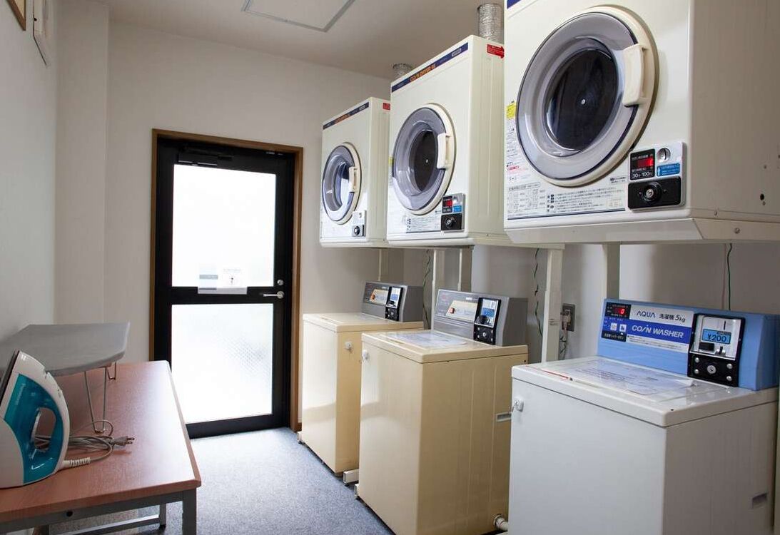 A laundry room with three front-loading washers and dryers, a table with an iron, and a door leading outside.