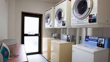 A laundry room with three front-loading washers and dryers, a table with an iron, and a door leading outside.