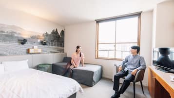 Habitación de hotel con cama, sofá, escritorio con televisor y ventana grande.