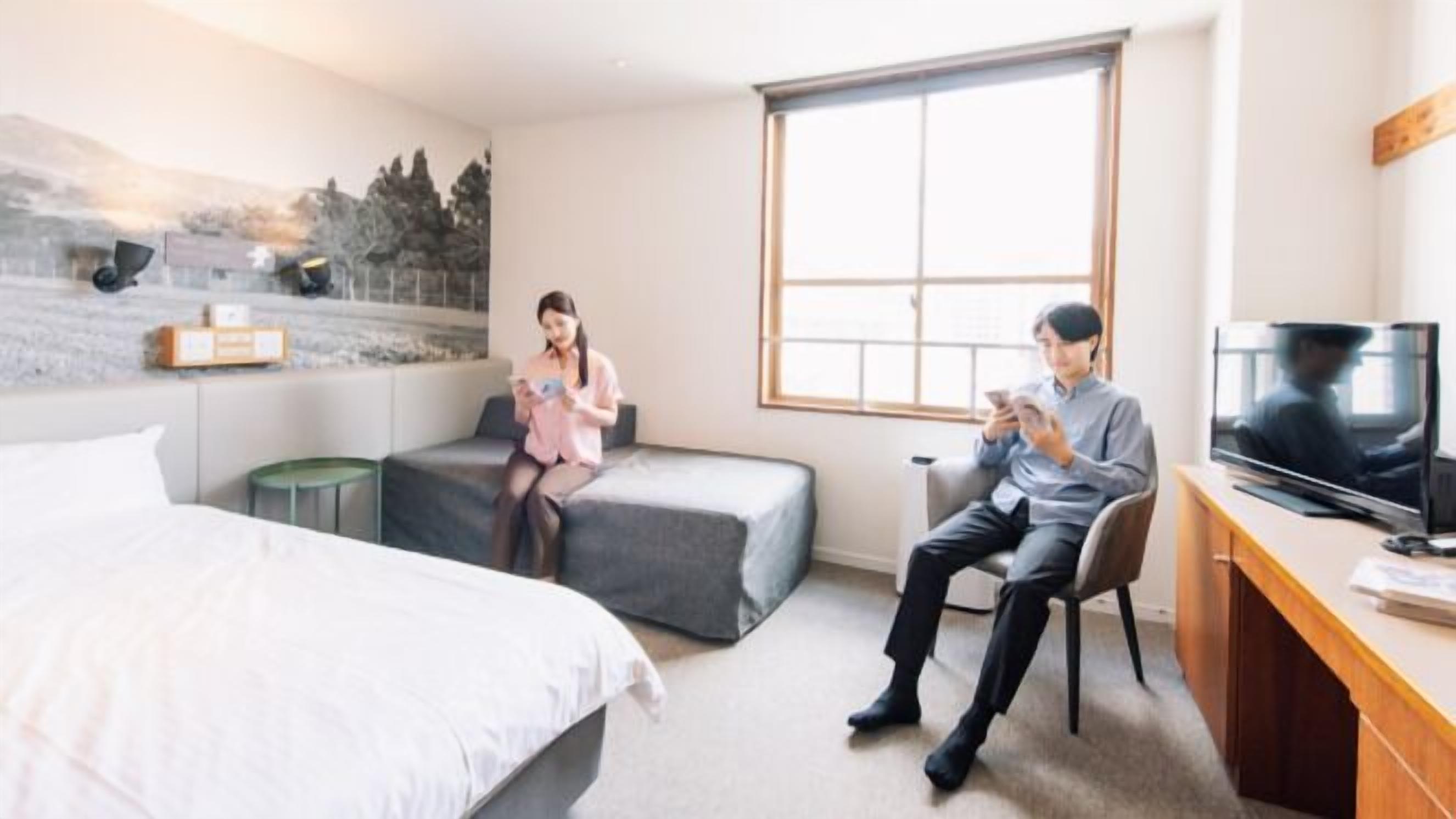 A hotel room with a bed, a sofa, a desk with a TV, and a large window.