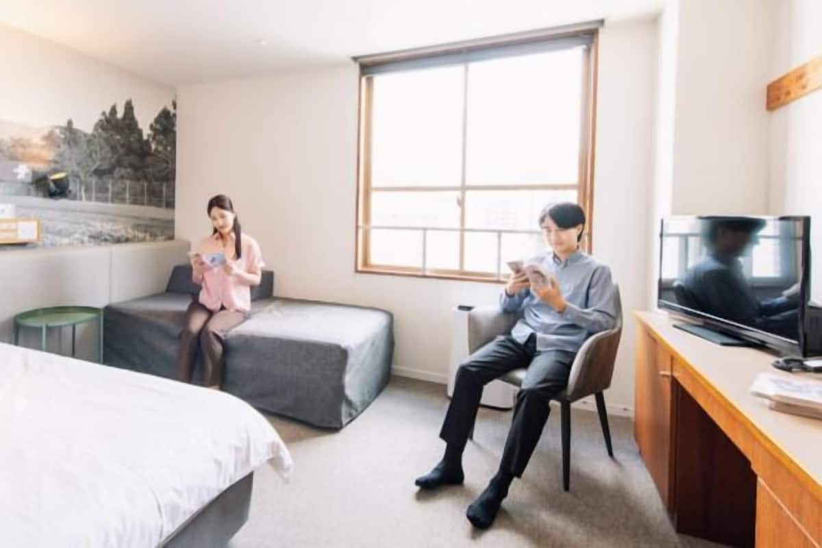 A hotel room with a bed, a sofa, a desk with a TV, and a large window.