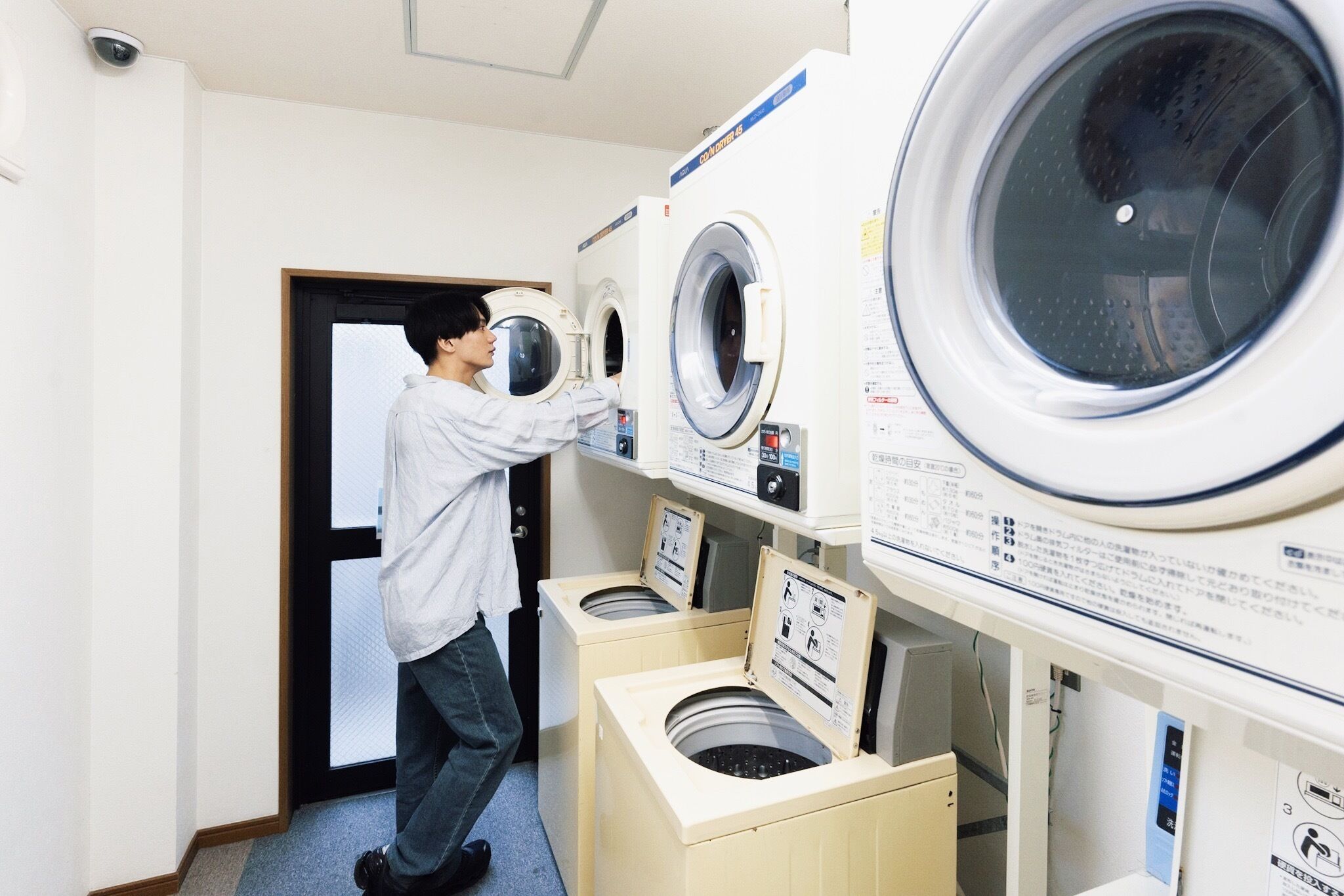 Un cuarto de lavado con varias lavadoras y secadoras, una cámara de seguridad y una puerta.