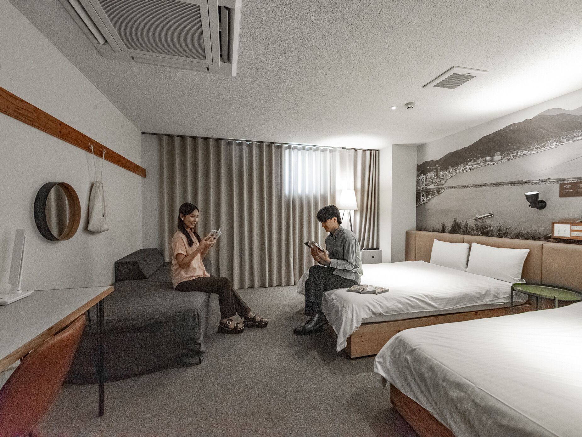 Quarto de hotel moderno com uma cama grande, uma mesa de escritório e um sofá. Há uma janela com cortinas, uma luminária na parede e vista para uma montanha.