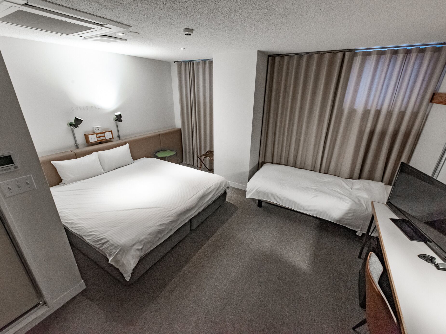 A hotel room with a large bed, a smaller bed, a desk with a laptop, and a television.