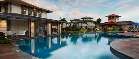 A swimming pool surrounded by buildings with outdoor seating and a clear sky.