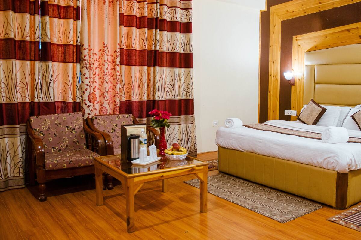 A hotel room with a bed, a chair, a table with a vase of flowers, and curtains with a floral pattern.