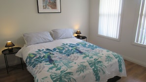 A bedroom with a bed, two nightstands, a lamp on each, a window with blinds, and a framed picture on the wall. - Relax in Comfort, Walking distance to beach (Mccracken)