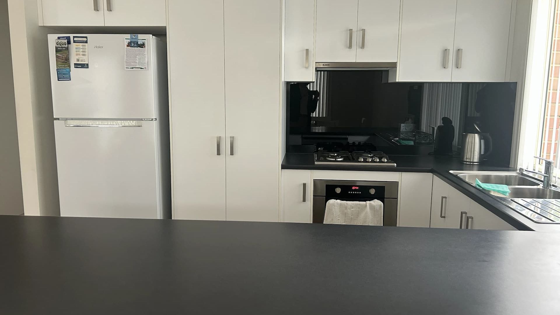 A modern kitchen with white cabinets, a stainless steel refrigerator, a black stove, and a dishwasher.