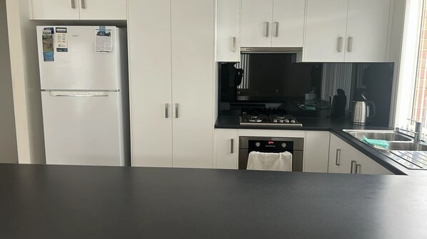 A modern kitchen with white cabinets, a stainless steel refrigerator, a black stove, and a dishwasher.