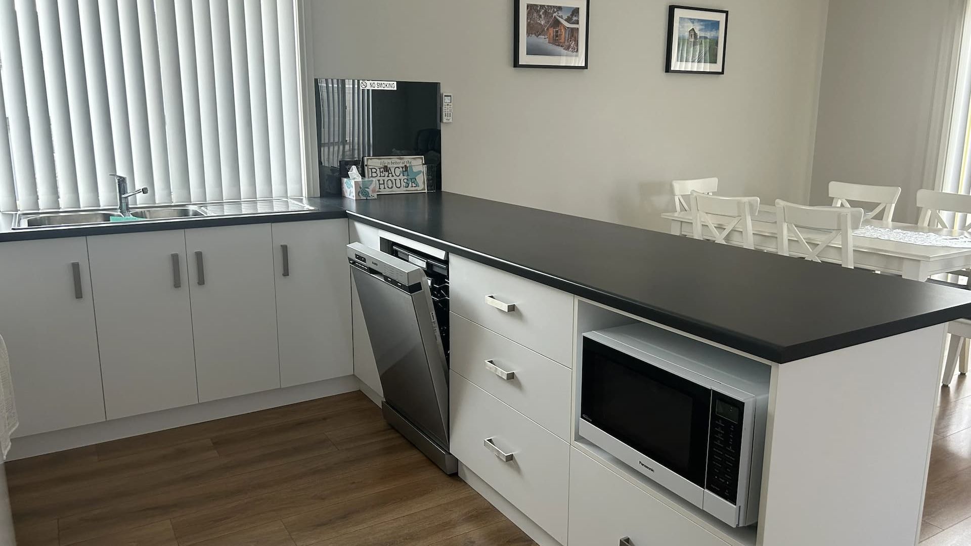 A modern kitchen with white cabinets, a black countertop, a dishwasher, and a microwave. There are two framed pictures on the wall.