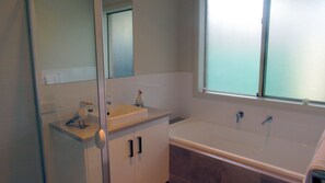 Une salle de bain avec un lavabo blanc, un miroir, une fenêtre et une baignoire.