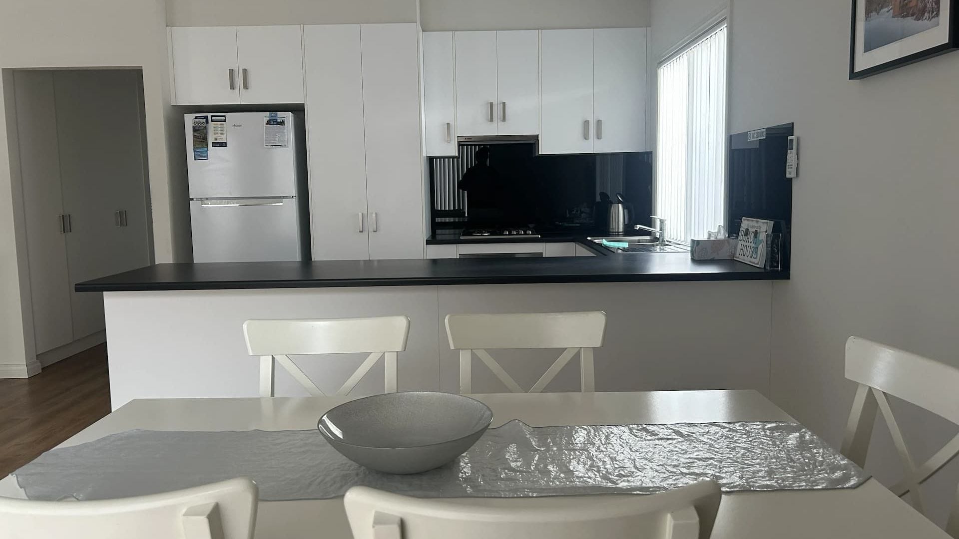 A modern kitchen with white cabinets, a black countertop, and a dining area with a table and chairs.