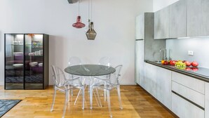 Eine moderne Küche mit einem runden Glastisch und transparenten Stühlen, einem eingebauten Backofen und einer Obstausstellung auf der Arbeitsplatte.
