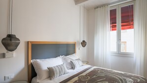 Ein Schlafzimmer mit Bett, Nachttisch, Lampe und einem Fenster mit Vorhängen.
