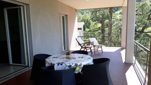 Ein Balkon mit Tisch, Stühlen, einer Topfpflanze und Blick auf Bäume sowie ein Gebäude im Hintergrund.